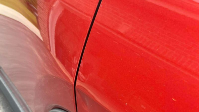 Glossy red car panel with reflective surface and door seam close-up