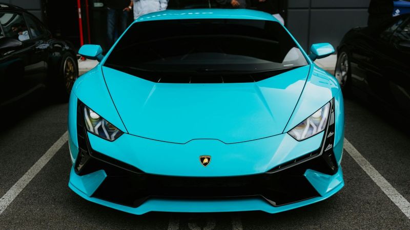 A striking turquoise Lamborghini front view, showcasing its sleek design and aggressive features, parked alongside other luxury cars.