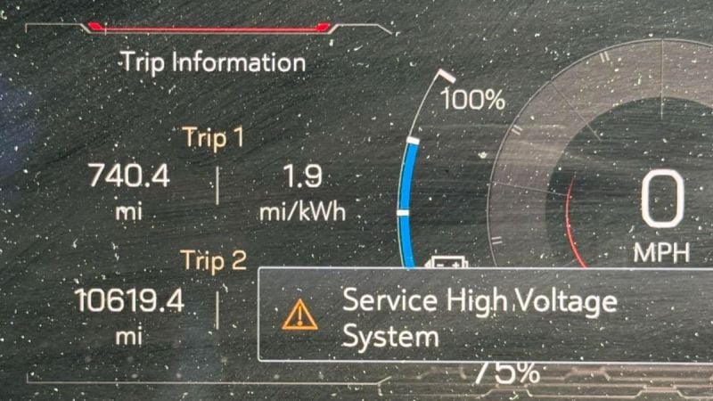 Dashboard of a GMC Sierra EV displaying trip information with a "Service High Voltage System" warning. Shows Trip 1 at 740.4 miles, efficiency 1.9 mi/kWh, and battery at 100%.