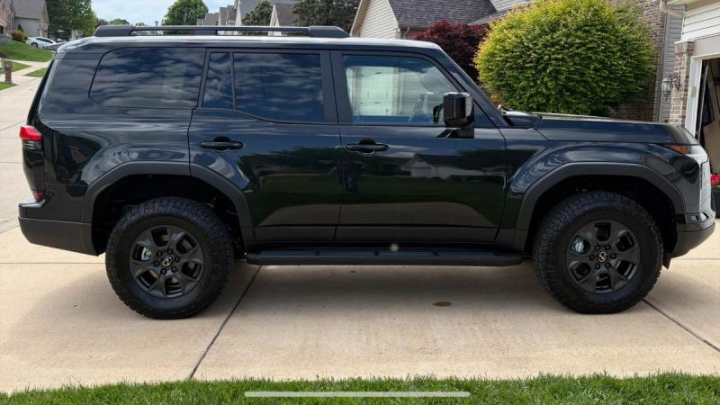 Black Lexus GX 550 SUV parked on suburban driveway, side profile with rugged off-road tires and dark alloy wheels