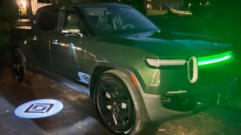 Green Rivian R1T electric truck parked at night with glowing green headlights and branded logo projection on ground