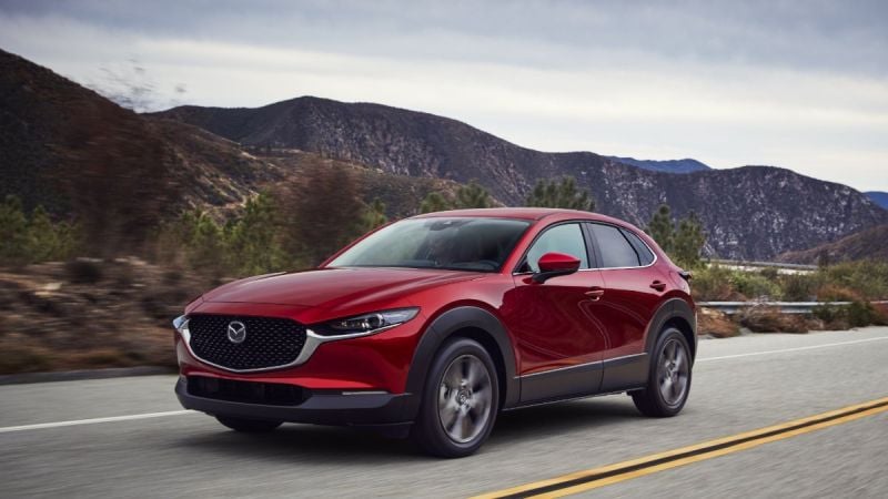 Red Mazda CX-30 compact SUV driving on a scenic mountain road, front three-quarter exterior view