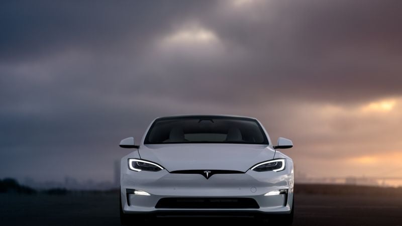 Front view of a 2025 white Tesla Model S against a dramatic cloudy sky, showcasing its modern design and iconic logo.