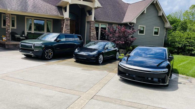 Three electric cars, Rivian, Tesla Model 3, and Lucid Air—are parked in a sunny driveway beside a modern house.
