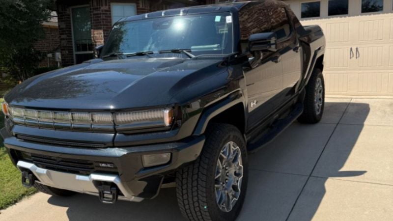 A black GMC Hummer EV truck with chrome accents and large tires is parked in a driveway. Sunlight reflects off the polished surface, creating a bold and powerful look.