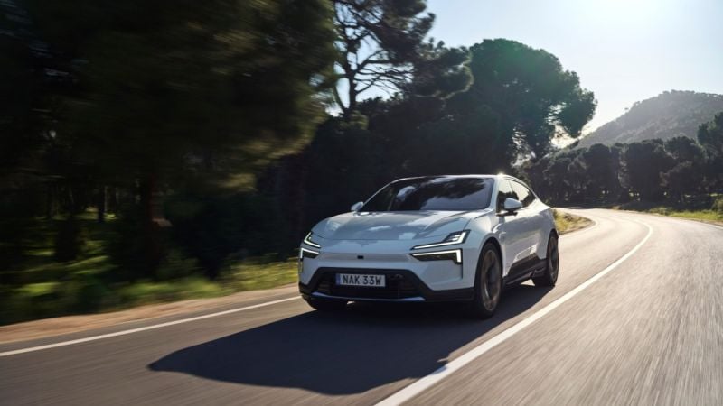 White electric SUV driving on curved mountain road surrounded by pine trees