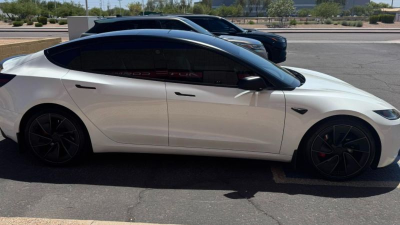 White Tesla Model 3 with black roof and wheels, side profile in parking lot with arid landscape background