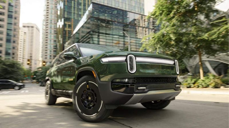 A sleek green electric SUV parked on a city street with modern skyscrapers in the background. Urban setting with greenery.