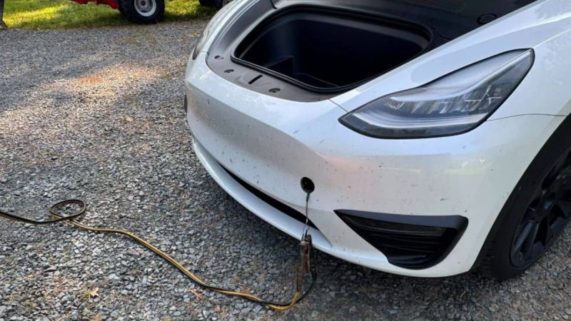 A white Tesla Model Y with the frunk open and cable attached during battery replacement process
