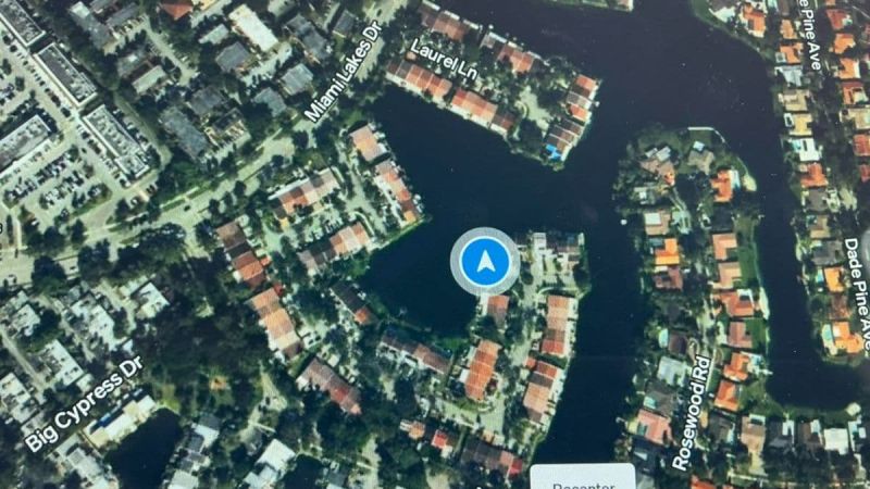 Aerial view of waterfront neighborhood with red-roofed houses, blue navigation marker, and winding water channels between residential areas.