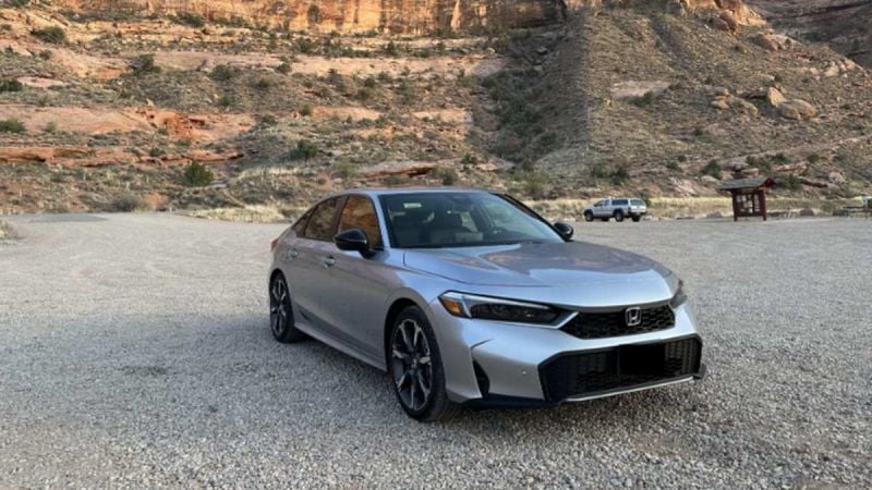 A silver Honda Civic parked on gravel with red rock formations in the background, showcasing a scenic desert landscape.