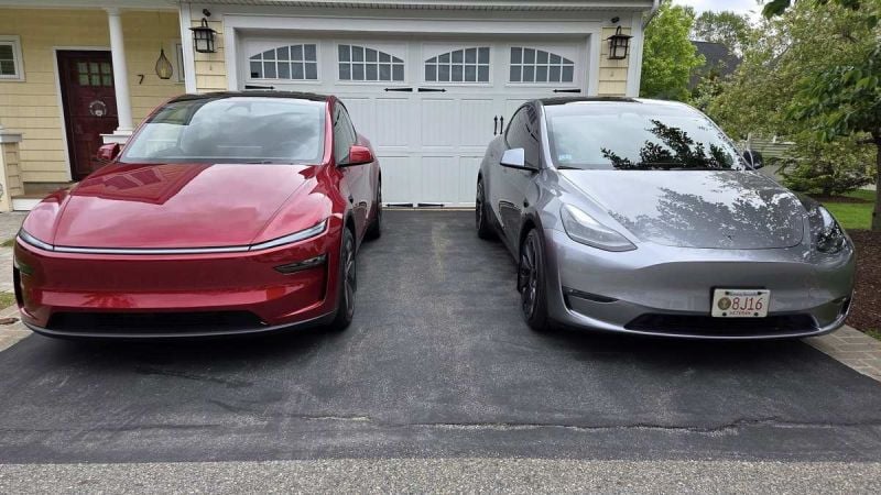 A red Tesla Model Y Juniper next to a silver Tesla Model Y parked in a driveway with a garage in the background.