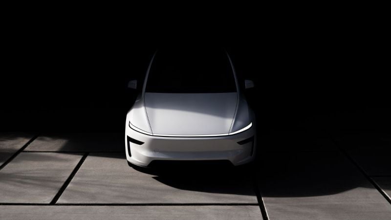 A sleek, modern white Tesla Model Y Juniper is illuminated against a dark background. The front view highlights its aerodynamic design and minimalistic style. Shadows create a dramatic, futuristic tone.