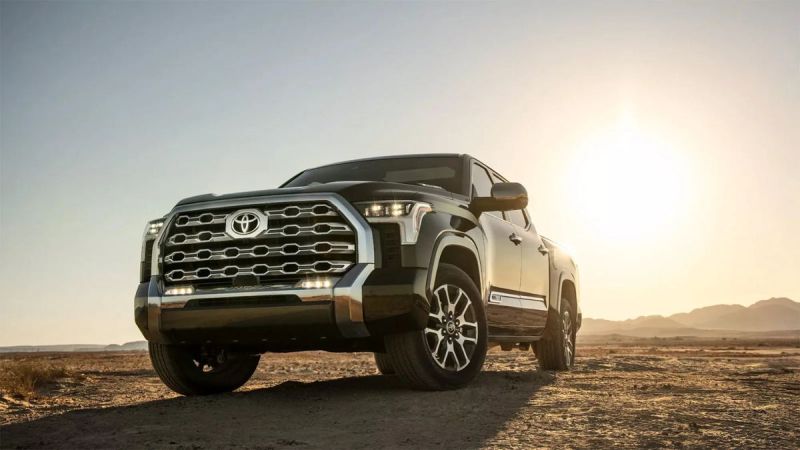A black 2022 Toyota Tundra is on a desert terrain with a striking grille is showcased against a bright sunset, evoking a rugged and adventurous tone.