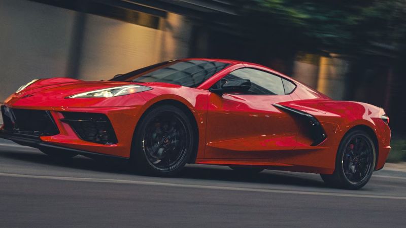 A red 2026 Corvette Stingray speeds down a city street at dusk. Motion blur highlights its aerodynamic design, reflecting a sense of power and excitement.
