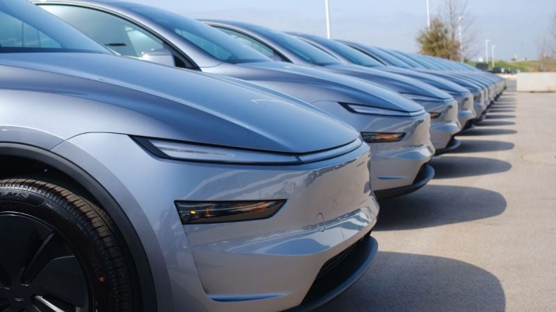 A row of silver Tesla Model Y's parked in a lot, showcasing their aerodynamic design and glossy finish under clear blue skies.