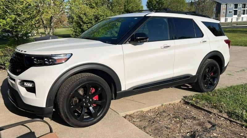 White Ford Explorer with black accents and wheels parked on suburban street with trees and grass
