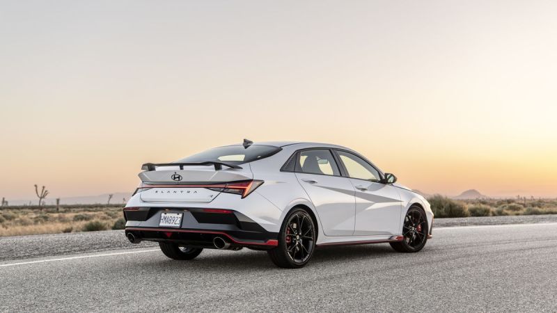 A 2025 White Hyundai Elantra N with sporty red accents and black rims is parked on a desert road at sunset, evoking a sense of adventure and freedom.