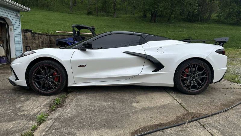 A sleek white Corvette Z06 parked on a driveway, showcasing its aerodynamic design and black alloy wheels against a green backdrop.