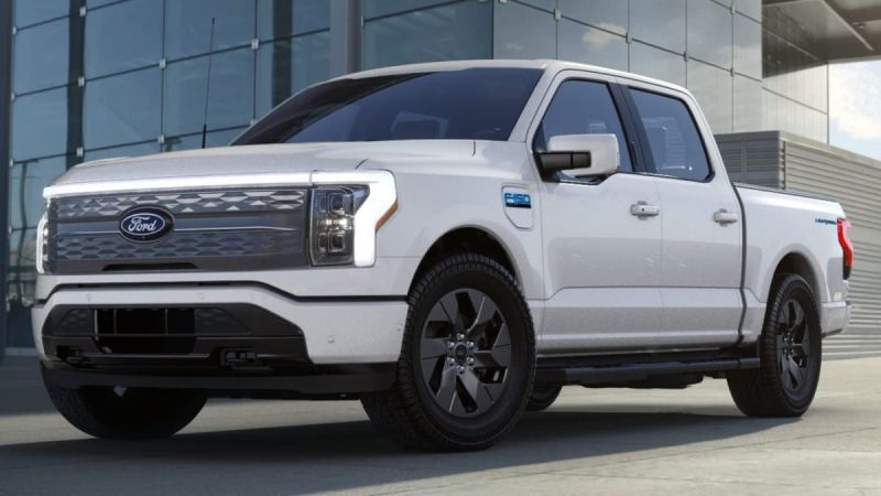 A white Ford F-150 Lightning truck parked in front of a modern building, showcasing its sleek design and prominent grille.