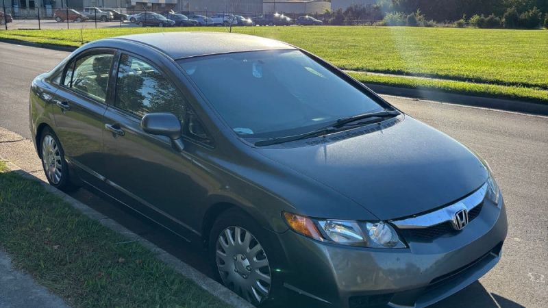 A dark silver 2009 Honda Civic is parked on a sunny street beside a green lawn. The car's exterior is shiny, and the setting is calm with a clear sky.