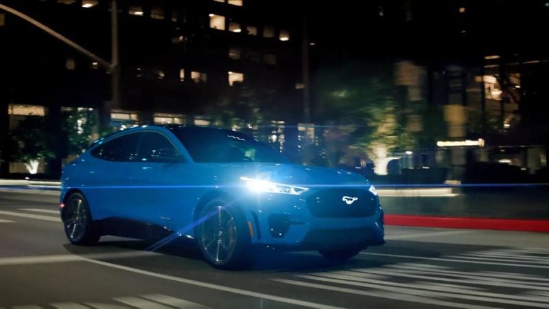 lue Ford Mustang Mach-E GT electric SUV driving on a highway at night, side profile view.