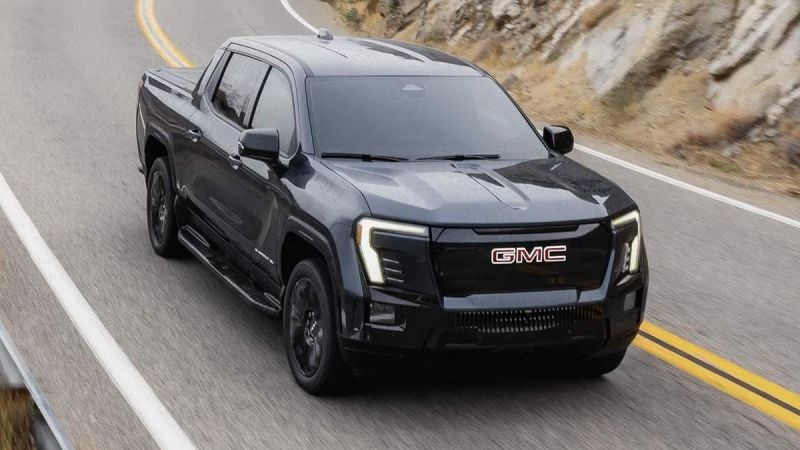 Black GMC Sierra EV electric pickup driving on a winding mountain highway, showcasing performance, LED lighting, and rugged design.