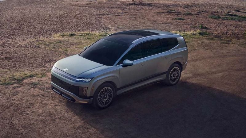 Aerial three-quarter view of a Hyundai IONIQ 9 electric SUV with a sleek gray exterior on a dirt overlook.