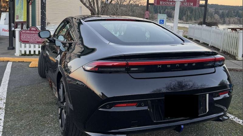 Rear view of a black Honda Prelude parked at a small town street near a gas station