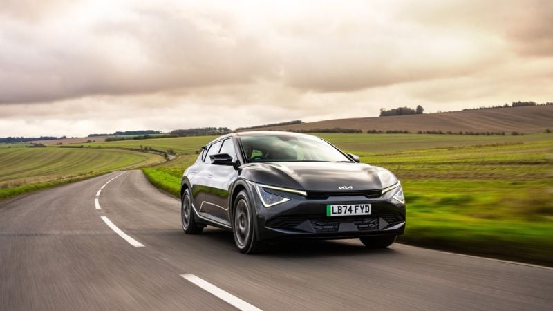 Kia EV6 electric crossover driving along a scenic rural highway under dramatic cloudy skies.