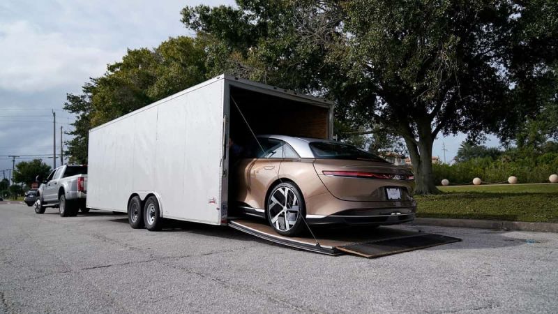 Image showing a gold Lucid Air being reversed out of an enclosed car trailer for customer delivery.