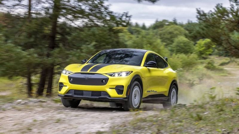 Bright yellow Ford Mustang Mach-E Rally driving on dirt trail through forest