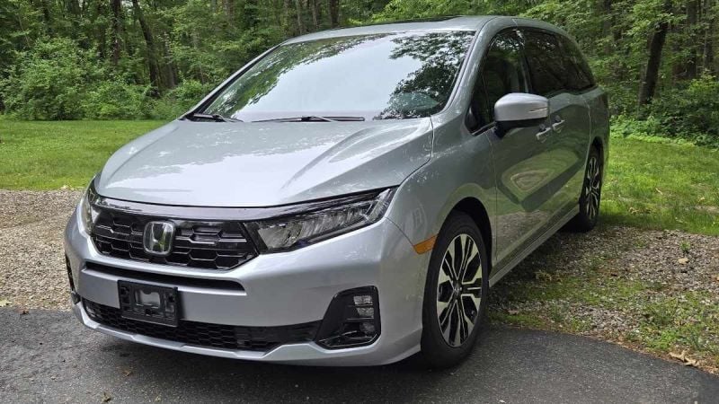 Silver 2025 Honda Odyssey Elite minivan parked on gravel path surrounded by lush green forest trees