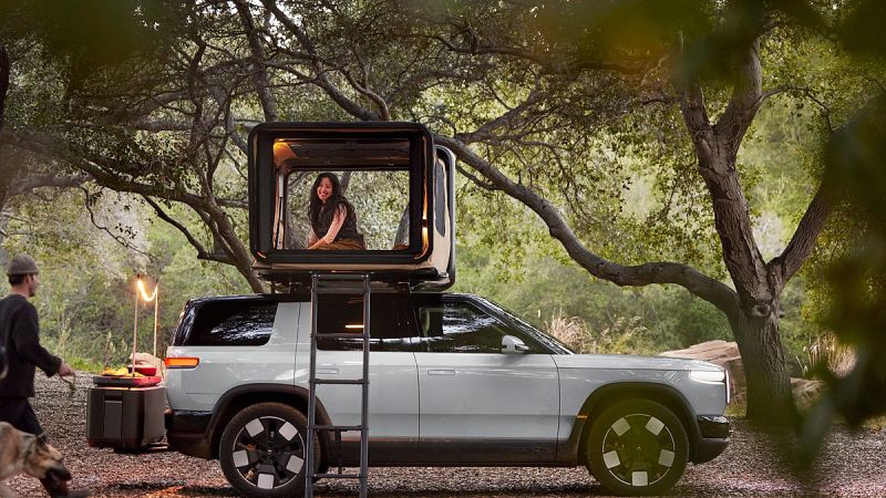A Rivian R2 all-electric SUV is shown in a tranquil camping scene