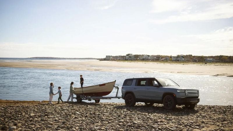 Rivian R1S towing a small fishing boat across a rocky beach at low tide, showcasing outdoor adventure and utility.