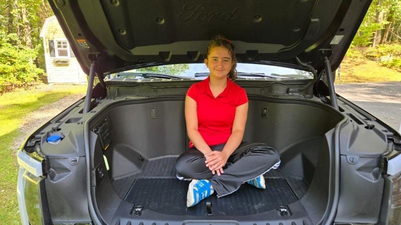 Image shows a young girls sitting inside of a Ford F-150 Lightning's frunk area