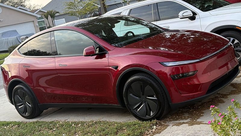 Red Tesla Model Y parked in residential driveway with suburban homes
