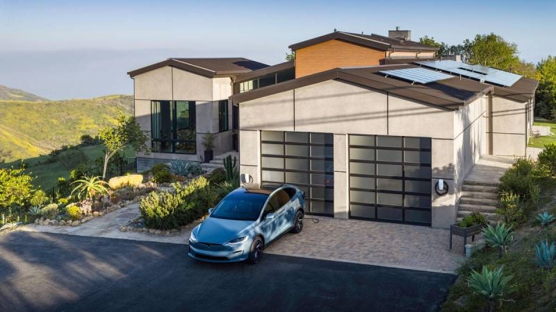 Tesla Model X parked in a modern hillside home driveway with solar panels and home EV charging station