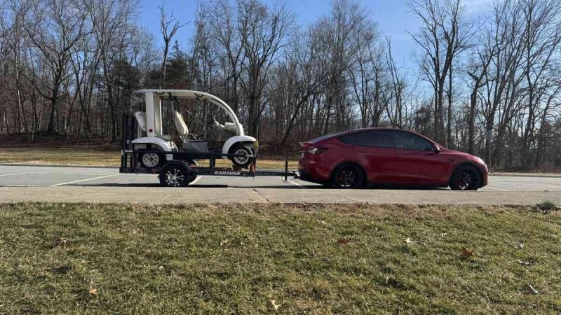 Red Tesla Model Y towing a trailer with a golf cart, electric SUV hauling in parking lot