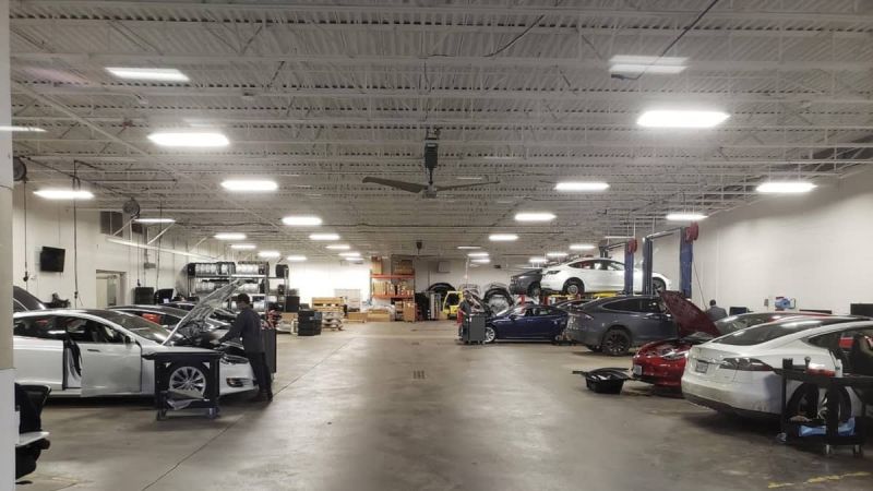 Tesla service center with multiple electric vehicles under repair in spacious, well-lit automotive workshop