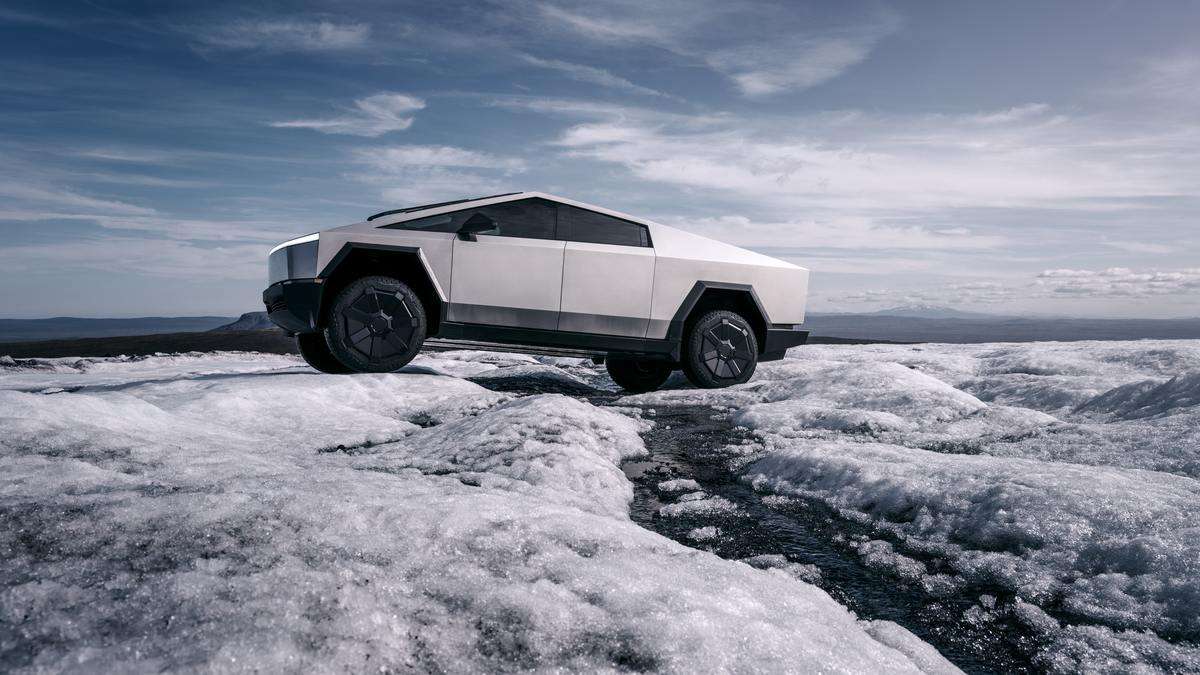 Tesla Cybertruck in stainless steel parked on an icy ridge, showcasing its angular design, off-road tires, and futuristic exterior in a cold landscape.