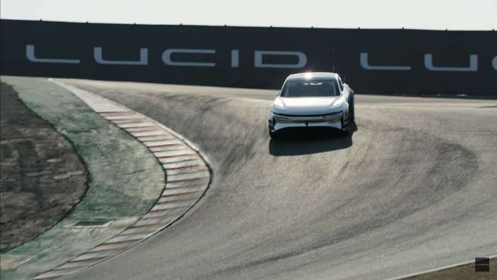 A prototype tri-motor Lucid Air enters the corkscrew corner at Laguna Seca, with Lucid bannering in the background.