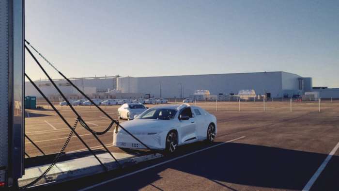 Image showing a Lucid Air wearing protective white wrapping being driven into a covered car transport trailer