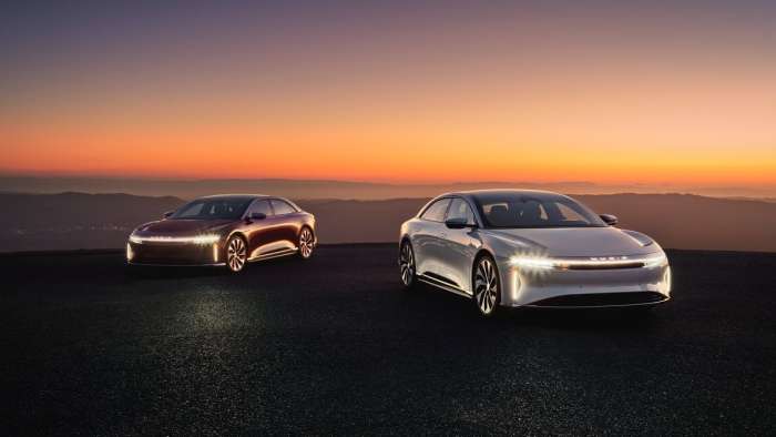White and red examples of the Lucid Air are pictured parked on a hilltop at sunset.