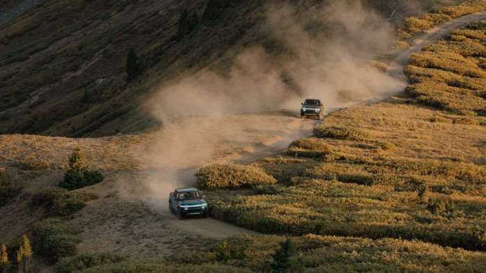A pair of Rivian R1T pickup trucks are pictured driving on a mountainside trail.