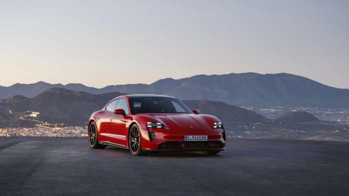 Image showing a red Porsche Taycan parked on a hill top in the mountains.