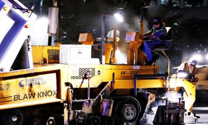 An asphalt paving machine begins paving while hot asphalt is still being loaded.