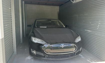 Black car with a covered hood parked in a narrow, corrugated metal garage.