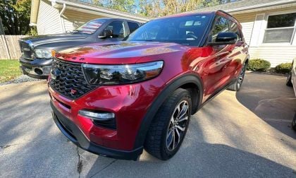 Red Ford Explorer ST parked in driveway next to black Ram truck.