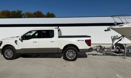 2021 Ford F-150 Platinum in Oxford White, side view, towing a trailer, parked outside white building with metal roof.